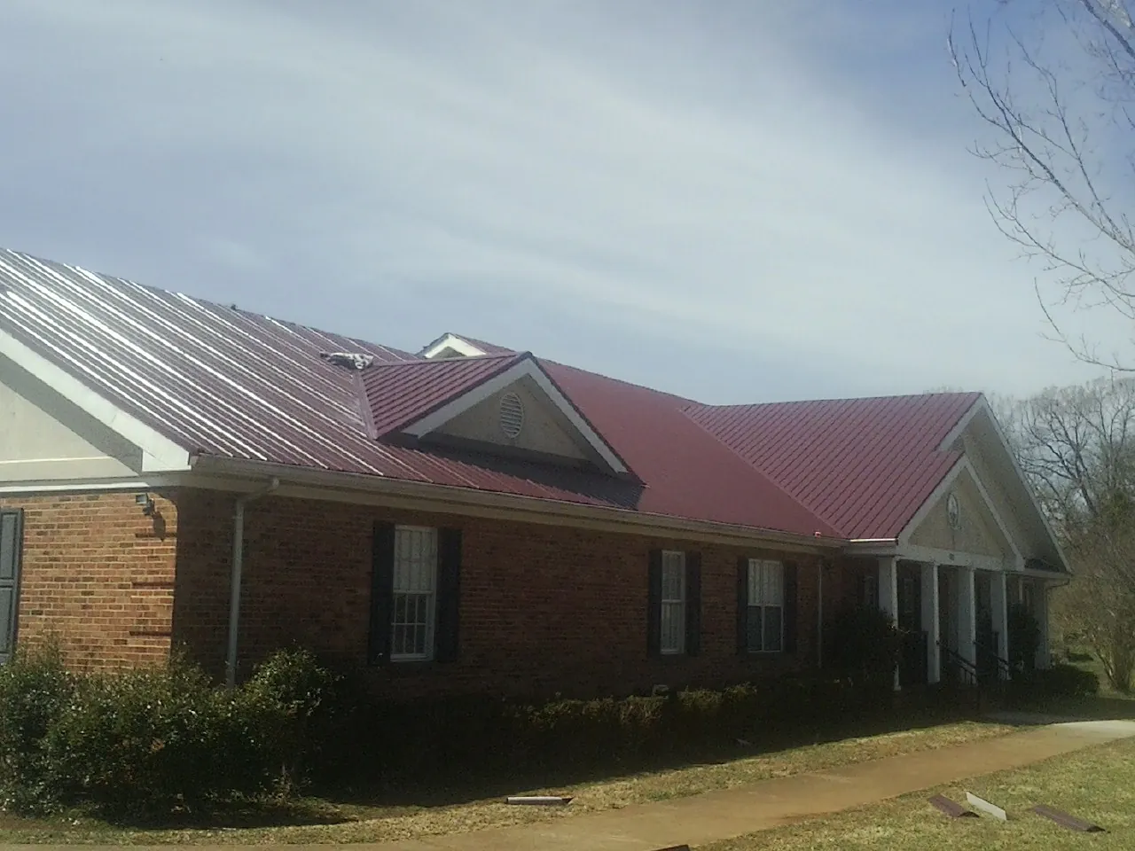 Red metal roof with gabled entries on a long brick building, from a Hail Damage Roof Repair job in Arrington