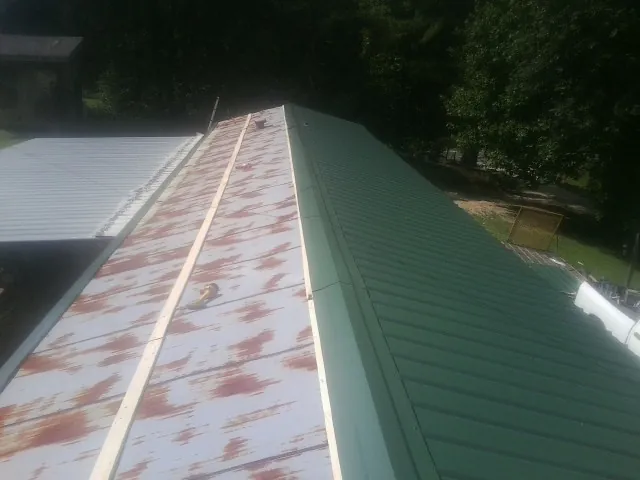 Old rusted panels beside newly installed green metal roofing — Wind Damage Roof Repair by Roofing Brothers in Arrington