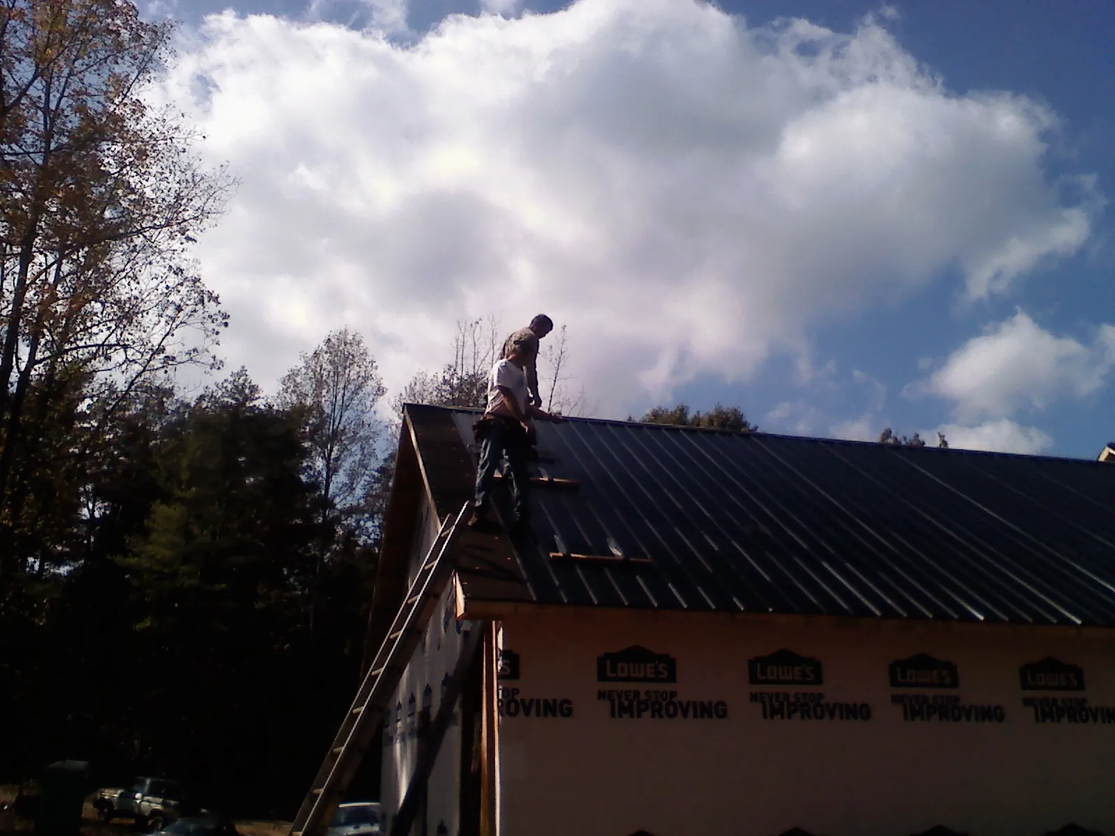 Roofer fastening dark metal panels high against a cloudy sky, from a Roof Inspection job in Arrington