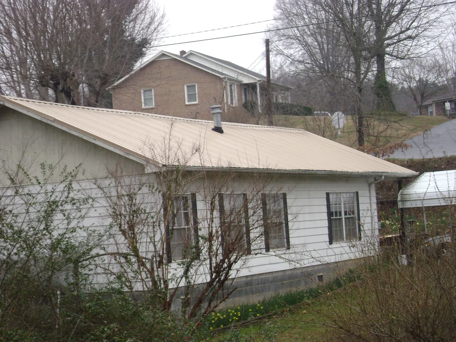Tan metal roof on a white sided house set into a hillside — Commercial Roofing by Roofing Brothers in Arrington