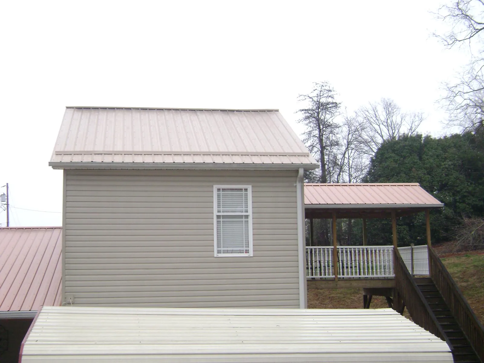 Tan metal roofs on a two story addition and attached porch, from a Roof Replacement job in Arrington